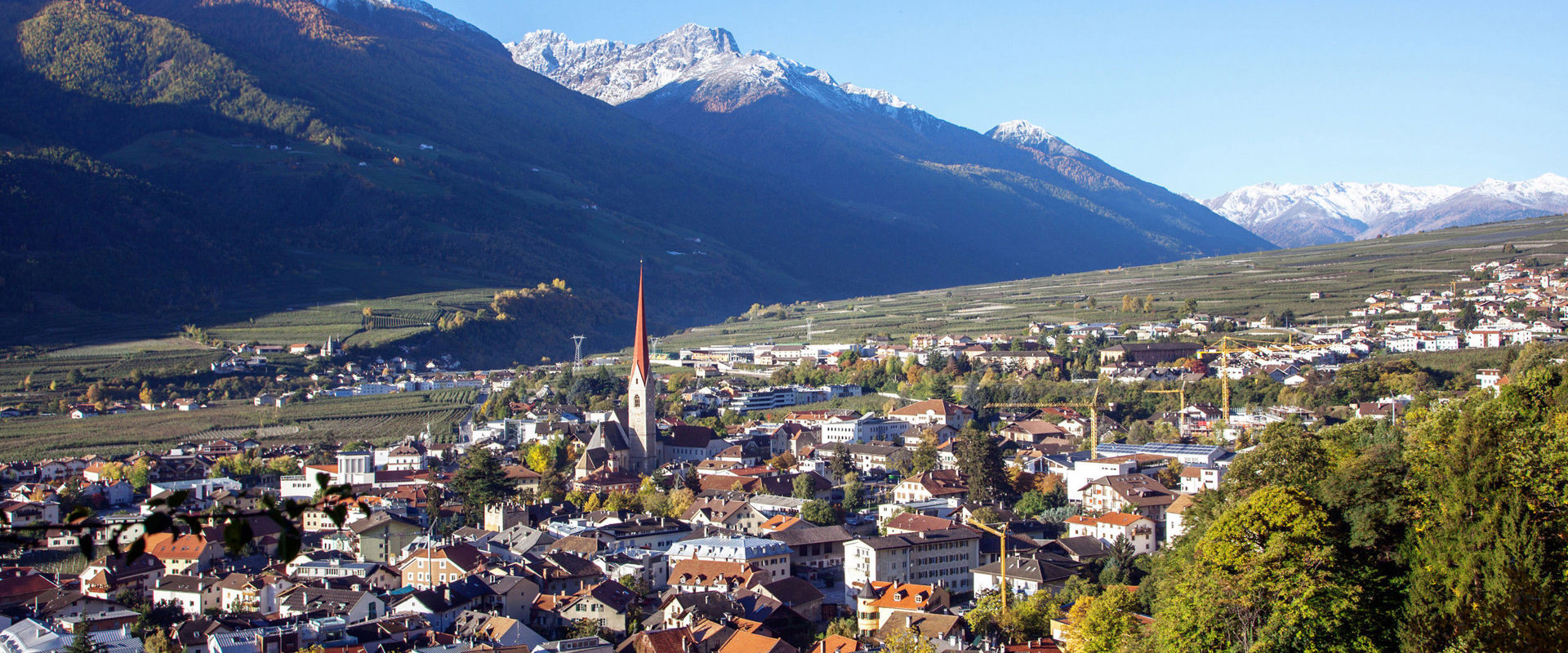Schlanders in Vinschgau View of Schlanders with houses, church tower, trees and mountains in the background.