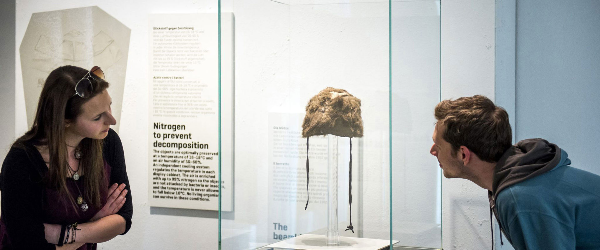 South Tyrol Museum of Archaeology 2 visitors admire an old cap in a showcase.