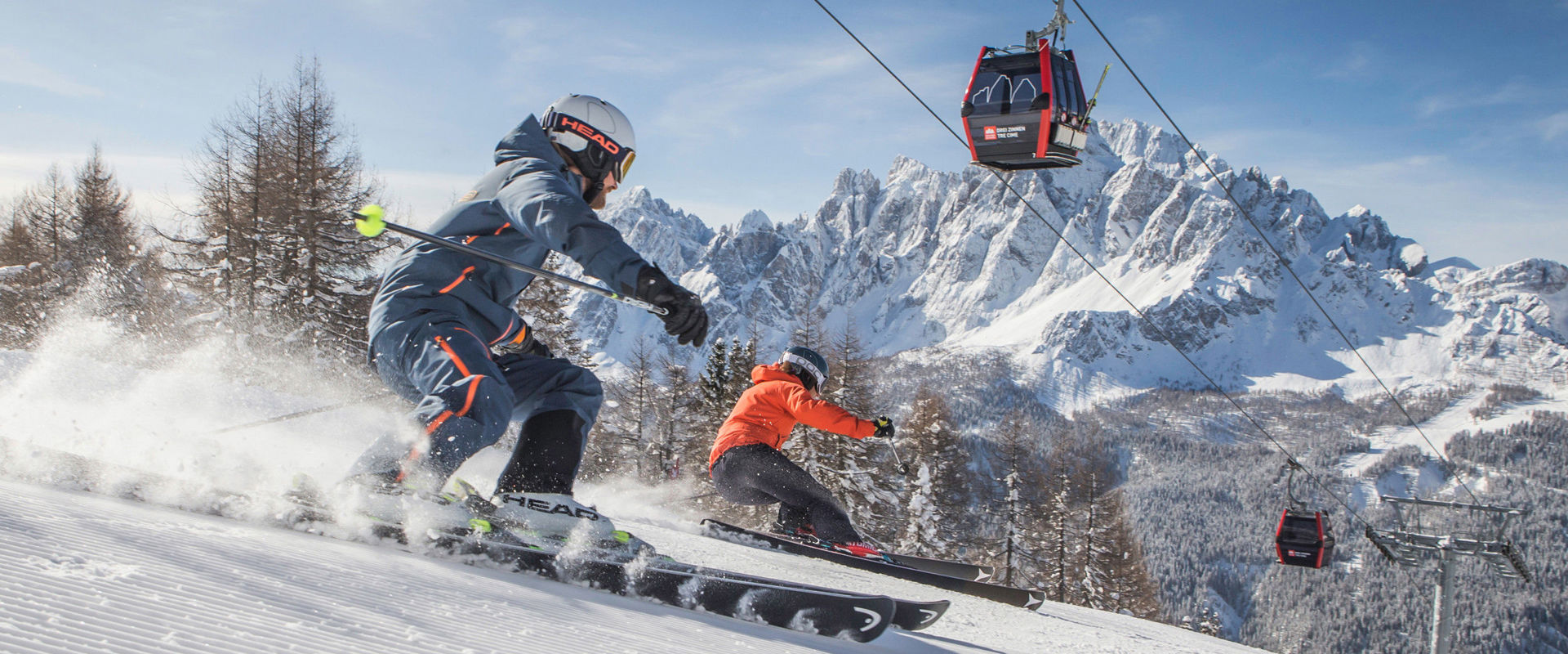 Two skiers on freshly groomed slope below the cable car.