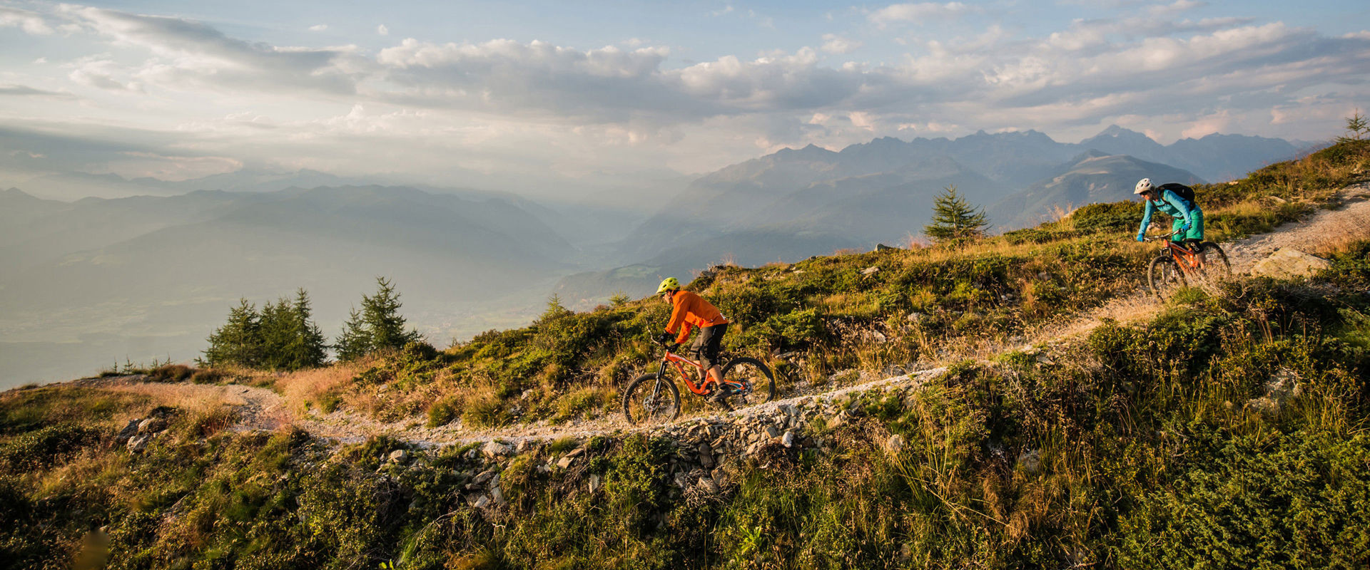 Bike descent Two cyclists ride down a narrow track down the mountain.