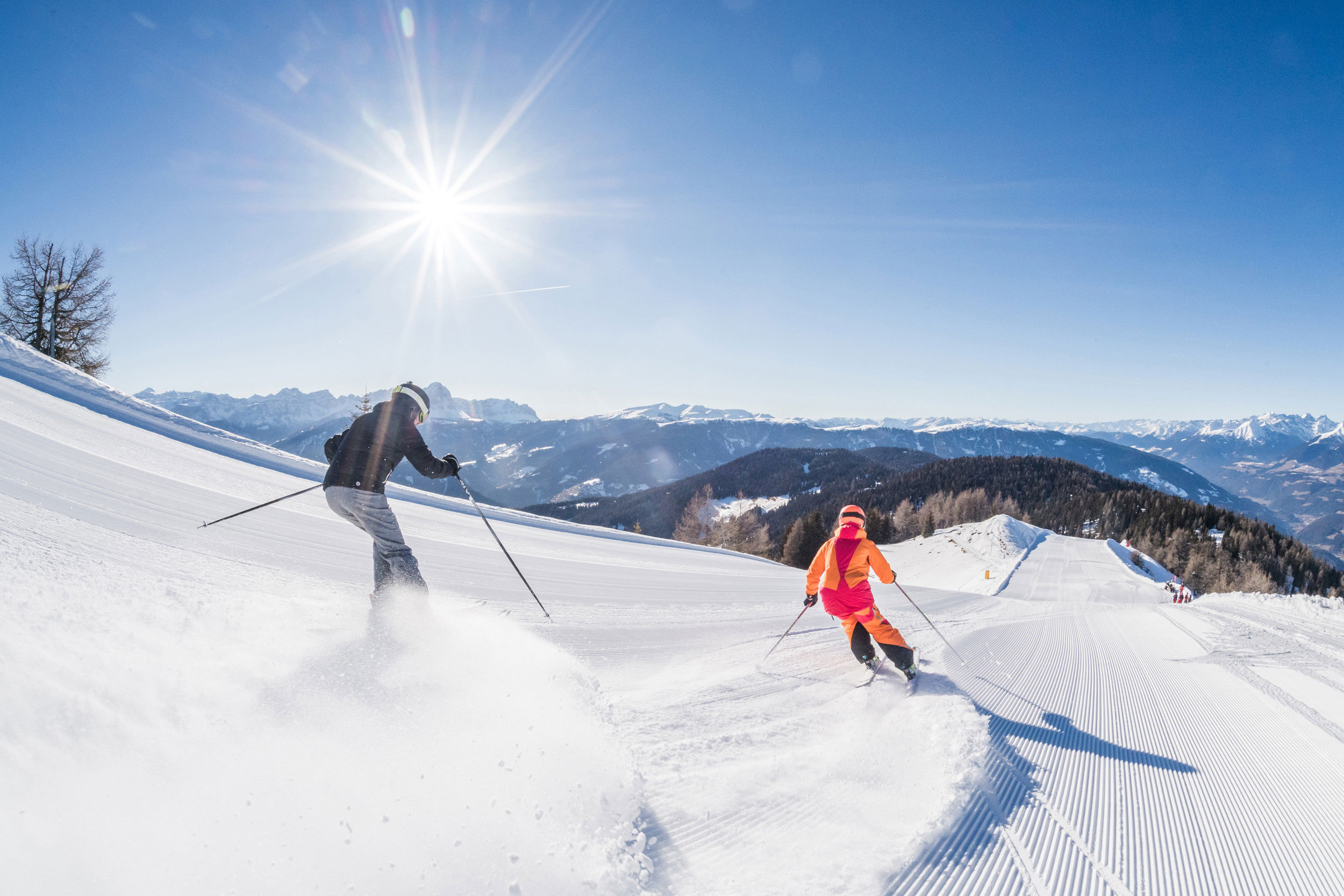Two skiers on a freshly groomed slope in bright sunshine.