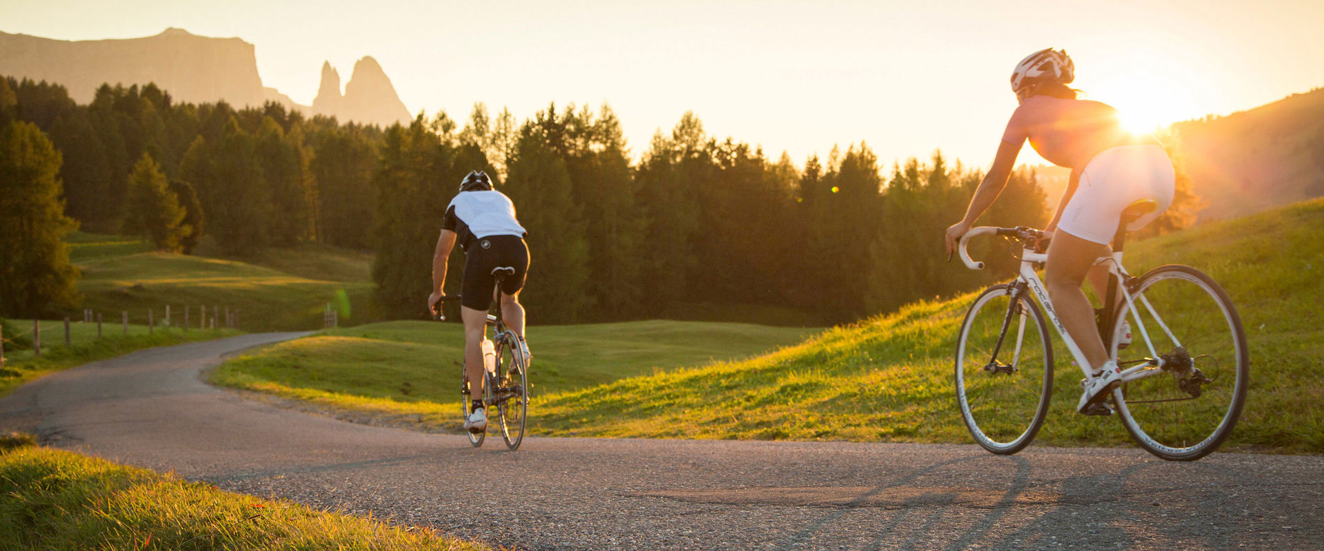 Road cycling on the mountain. 2 cyclists ride down the mountain during a breathtaking sunset.