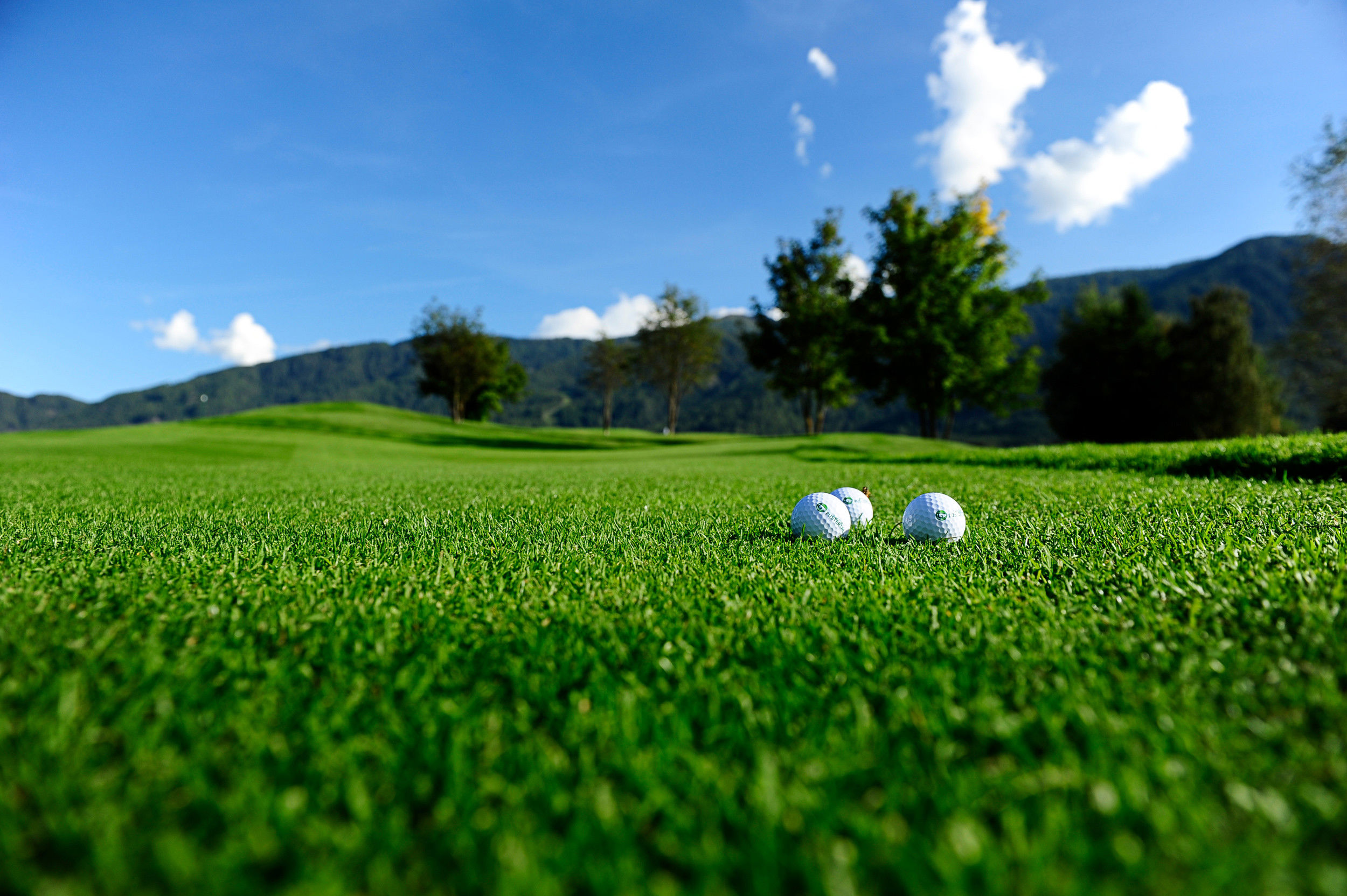 3 golf balls lie in the middle of the meadow on the golf course.