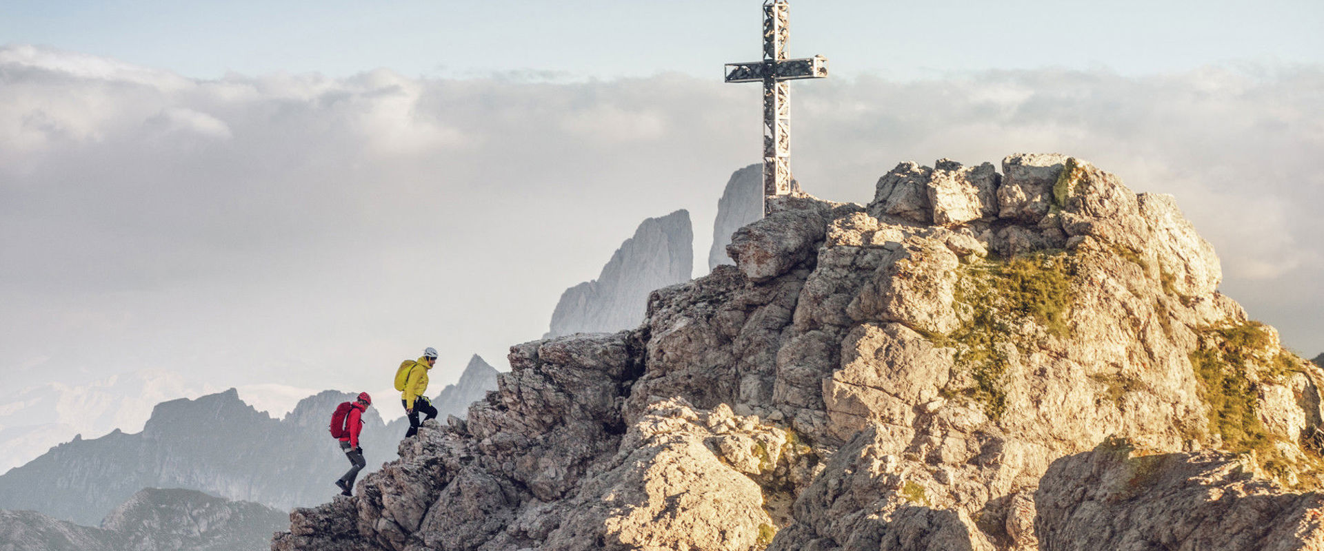 Two hikers reach the cross at the top of a mountain in Gröden.