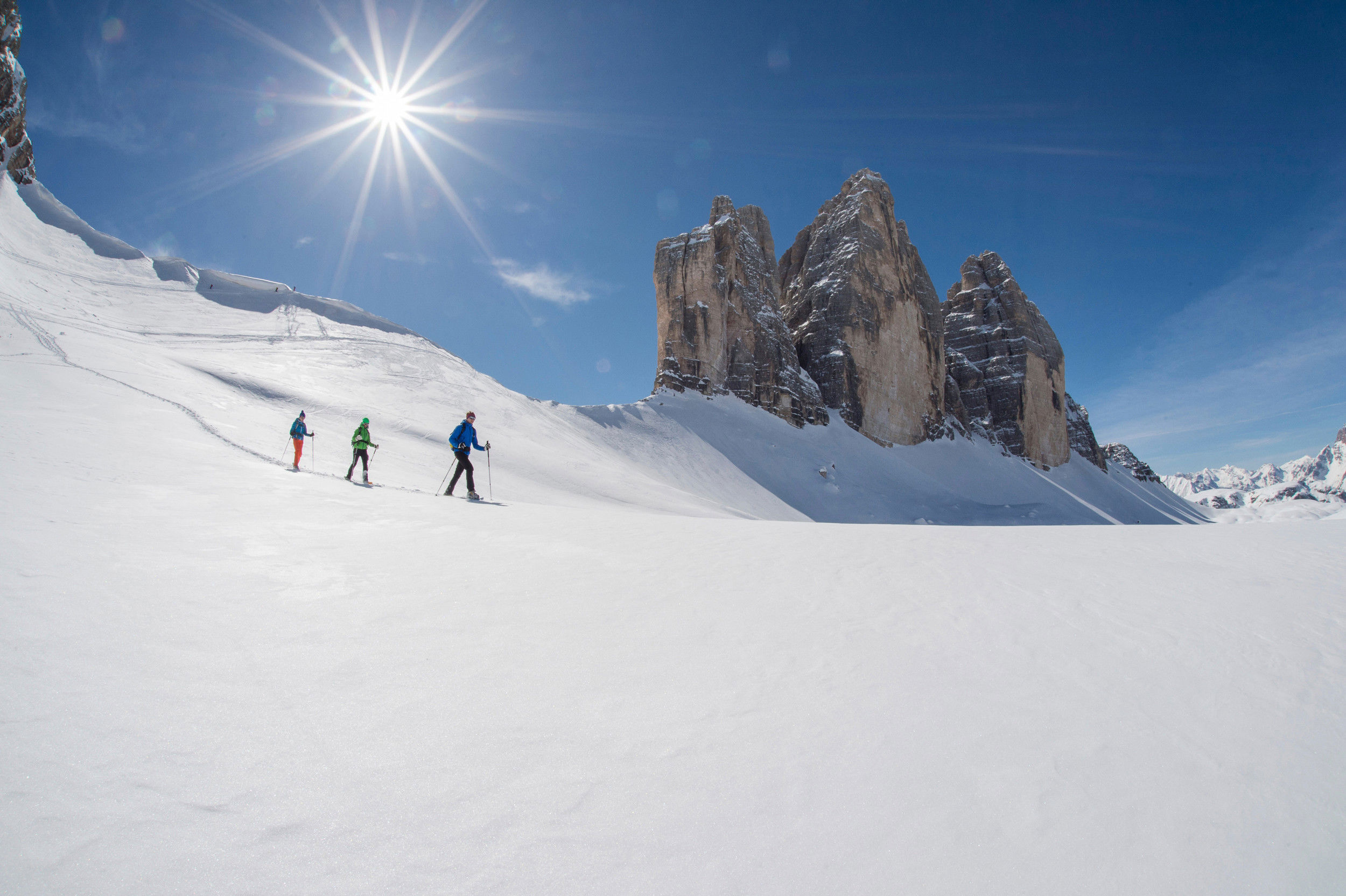 Snow-covered winter landscape around the Three Peaks. Below the mountain 3 people pass with their ski.