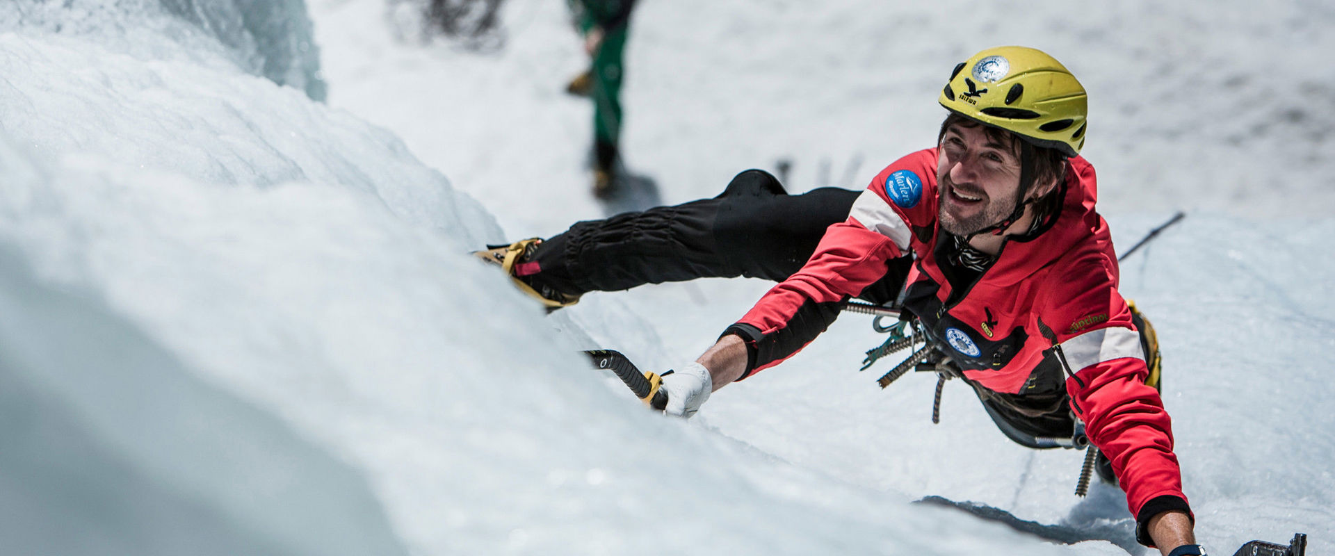 Ice climber with ice axe, rope and helmet climbing up an icy waterfall.