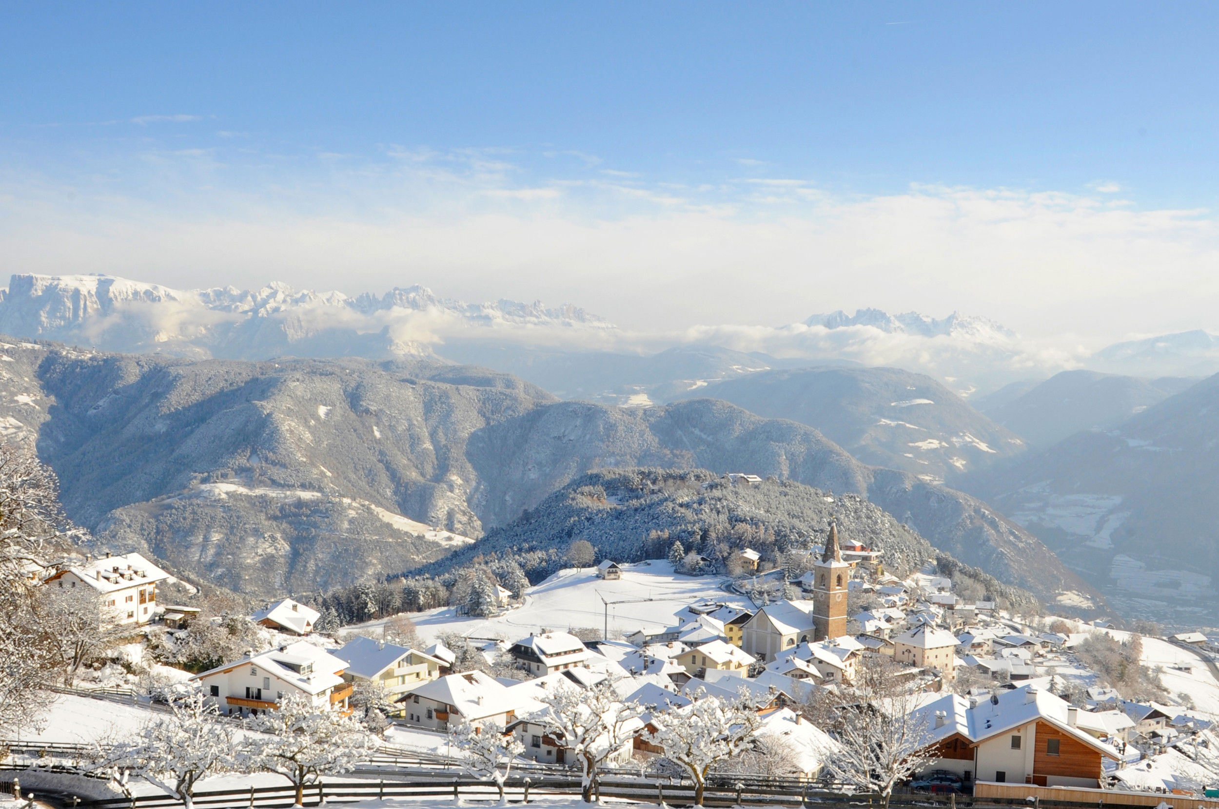 Jenesien from above in winter with village centre and church, Dolomites in the background