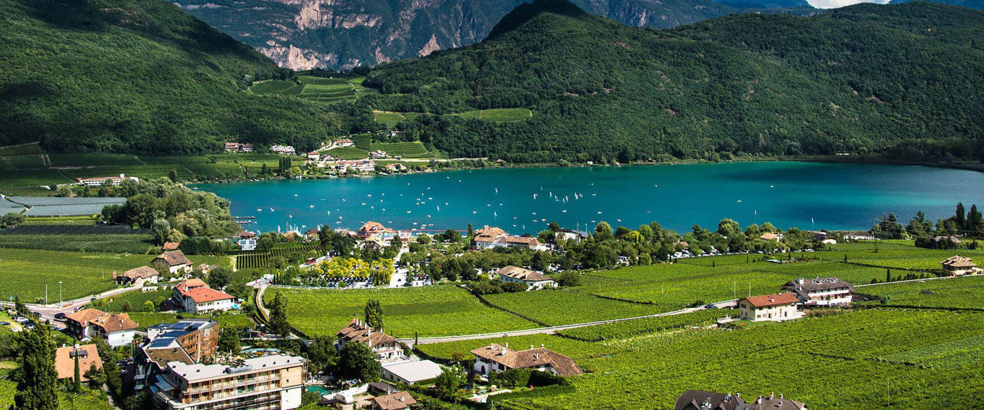 St. Josef am See and Lake Kaltern The turquoise blue Lake Kaltern amidst vines, houses and trees.