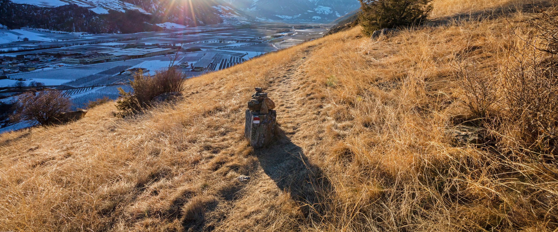Vinschger Sonnenberg Dry grassy slope and snow-covered meadows in the shade on the opposite side of the mountain.