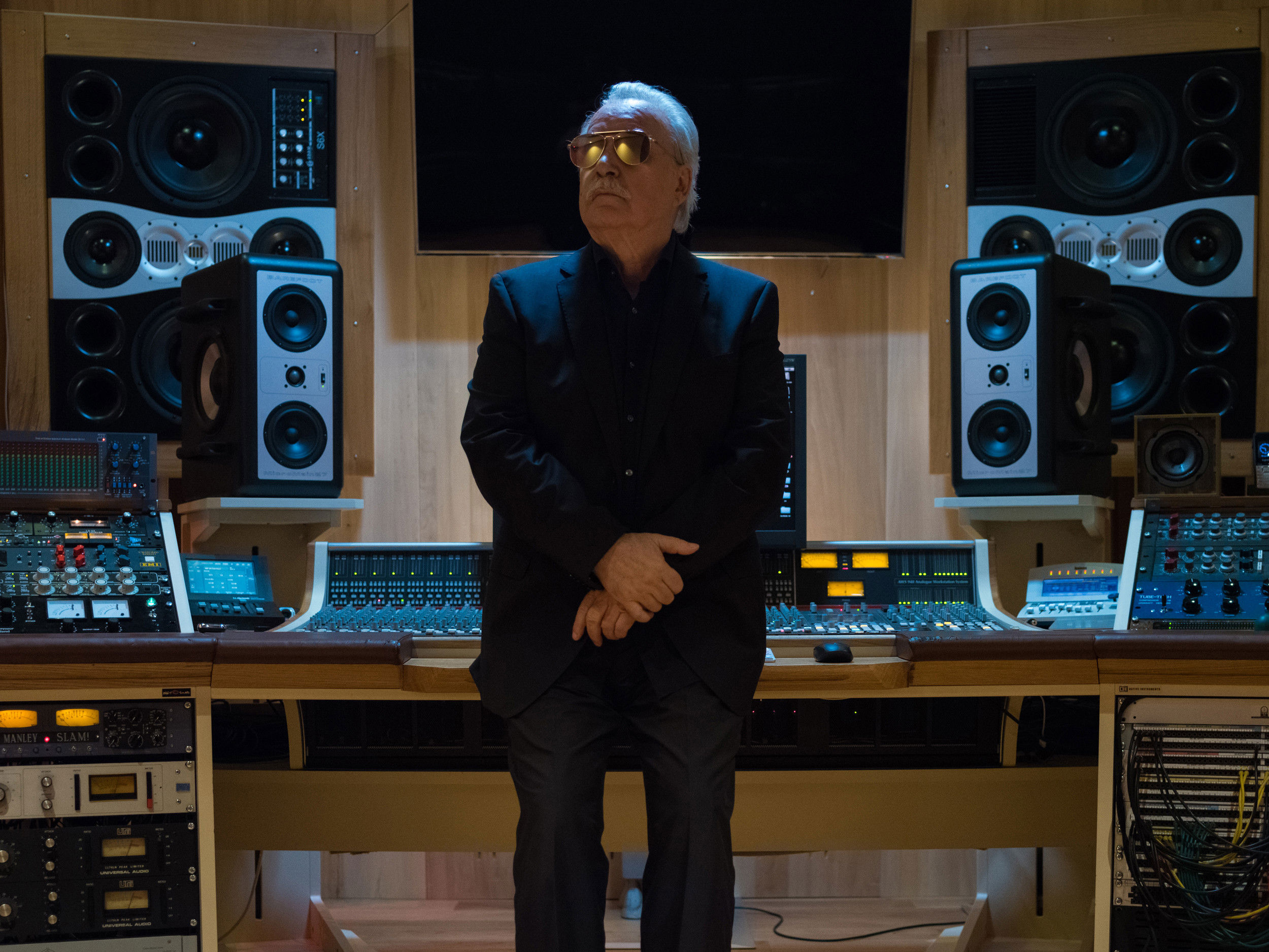 The elderly music producer sits at the mixing desk in a recording studio.