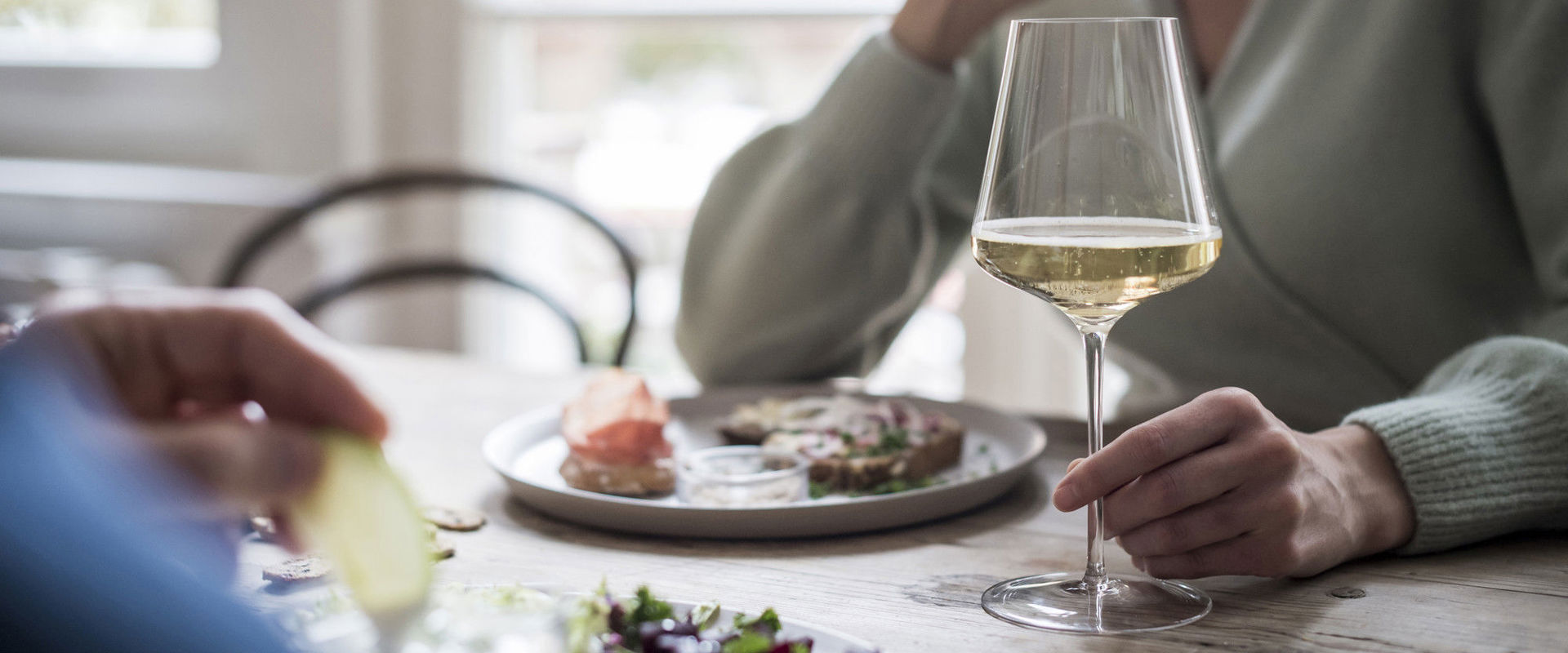 Eating habits Woman sitting at the table eating and holding a glass of white wine.