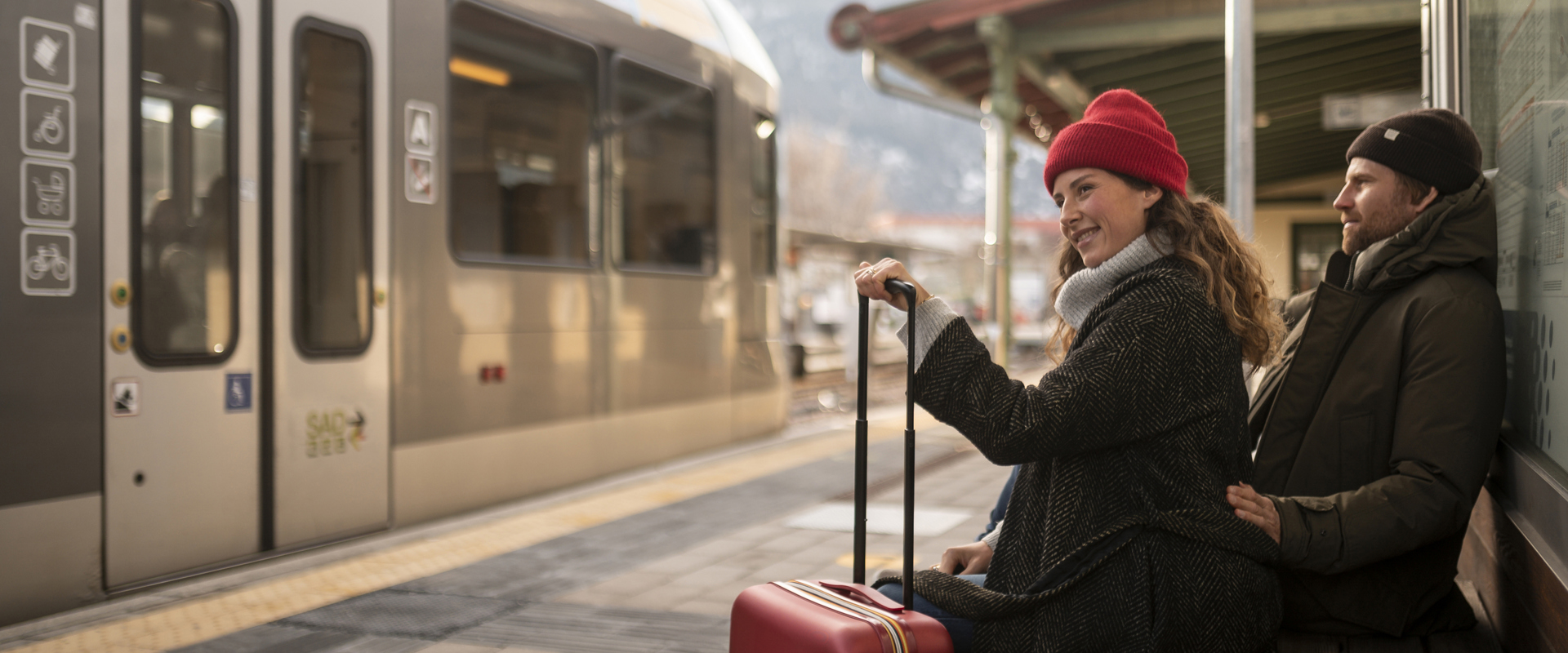 Arrival by train Couple with suitcase sitting at the railway station, train in the background
