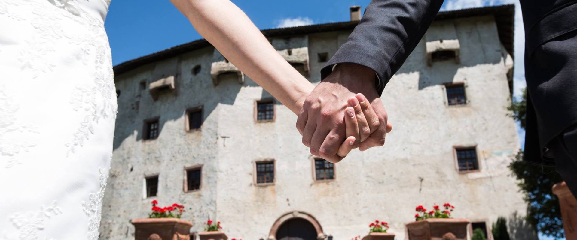 A bride and groom hand in hand in front of Castel Katzenzungen